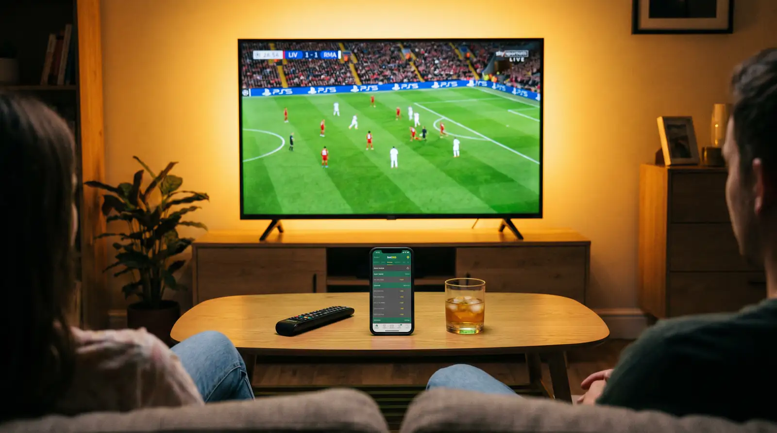 Living room setup with football streaming on television and betting app on a phone